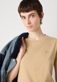 Beige katoenen t-shirt met geborduurd "BOSS" logo, gecombineerd met een denimjack met contrasterende blauwe tinten en knoopdetails.