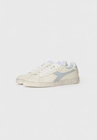 Klasiski sporta apavi off-white un gaiši zilā krāsā, ar zamša augšpusi, noapaļotu purngalu, šņorēšanas dizainu un strukturētu gumijas zoli.