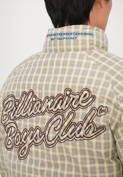 Postavljena bež i kremasto karirana jakna s velikim smešnim izvezenim natpisom "Billionaire Boys Club" na leđima, s plavim tekstom na ovratniku.