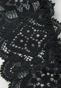 Tissu en dentelle noire présentant des motifs floraux complexes et des bords festonnés, avec une finition texturée et un design à tissage ouvert.