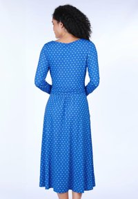 Blaues langärmliges Kleid mit tailliertem Schnitt und fließendem Rock, mit grünen Punkten und rundem Ausschnitt. Glatter, elastischer Stoff.