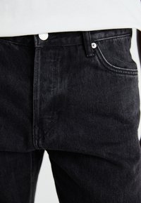 Jeans din denim negru expuși, având un design clasic cu cinci buzunare, închidere cu buton și cusături vizibile pe cusături.