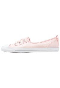 Zapatilla de lona de caña baja en rosa claro con suela de goma blanca, punta y tres ojetes plateados para los cordones, mostrada desde un lateral.