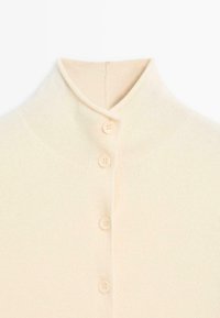Stickad tröja i mjuk krämfärg med hög krage, prydd med fem matchande knappar och en slät, texturerad yta.