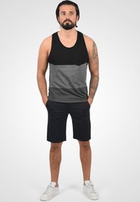 Sort og grå tanktop med lomme, der har et horisontalt farveblokdesign. Kombineret med mørke shorts og hvide sneakers.