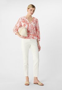 Bluse mit floralem Druck in Pink und Orange, weiße, figurbetonte Hose, beiger Bag und geflochtene Sandalen. Das Design verfügt über lange Ärmel und einen V-Ausschnitt.