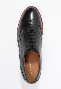Chaussure oxford en cuir noir avec des empiècements en brogue, bout arrondi, lacets à l'avant et semelle contrastante marron. L'intérieur présente un nom de marque en relief.