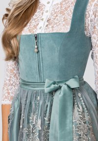 Green velvet dirndl with lace sleeve, silver embroidery on tulle skirt, and satin bow at the waist; features a decorative zipper.