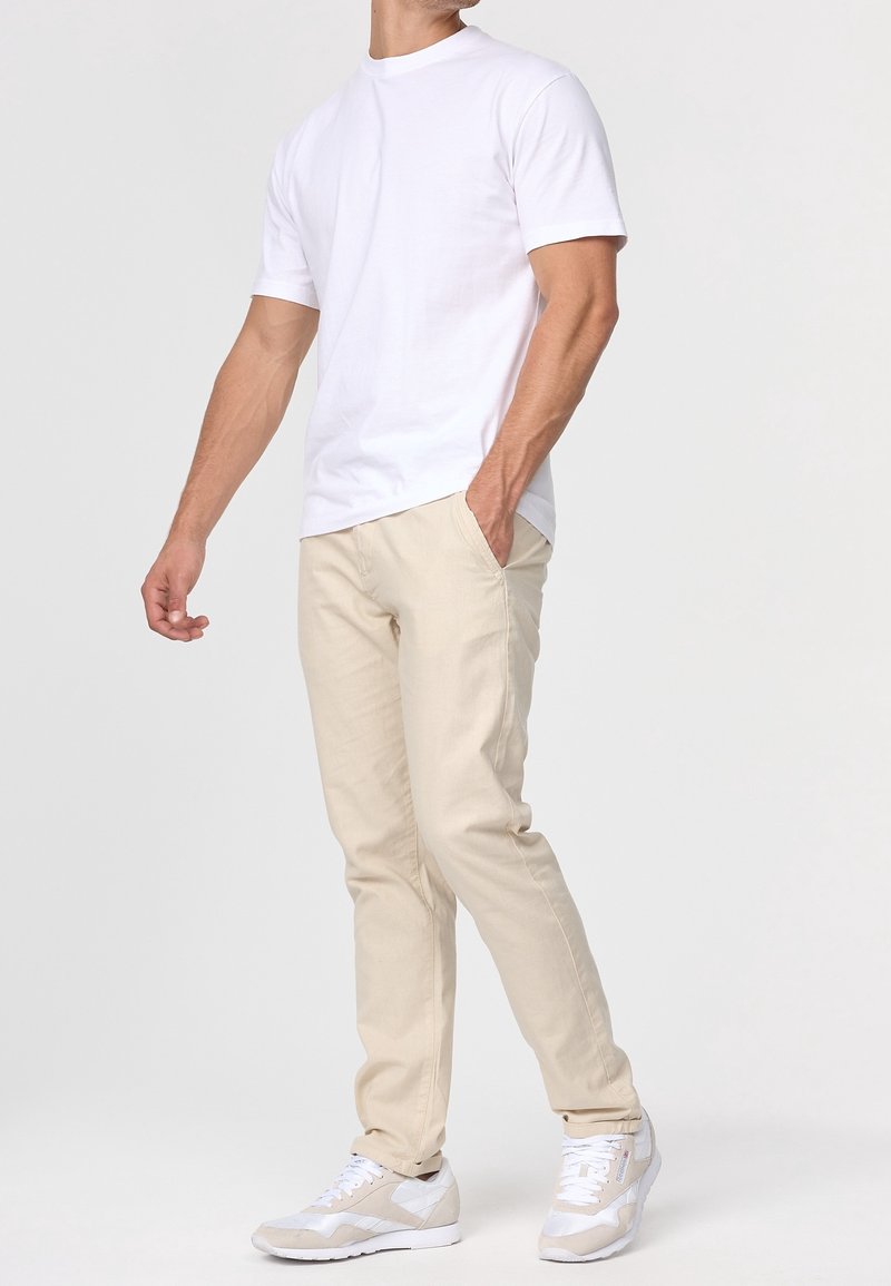 Hvid bomulds t-shirt, beige slim-fit bukser og lysegrå sneakers. Outfittet har et afslappet design og en komfortabel pasform.