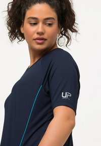 Camiseta deportiva navy de mangas cortas, con tejido texturizado, detalles en azul claro a lo largo de los costados y un logotipo plateado de "UP Sports" en la manga.