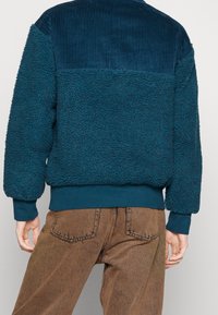 Tepelfärgad tröja i texturerad fleece med en överdel i kordflors. Har ribbade ärmslut och nederkant, vilket ger en bekväm passform och kontrast i material.