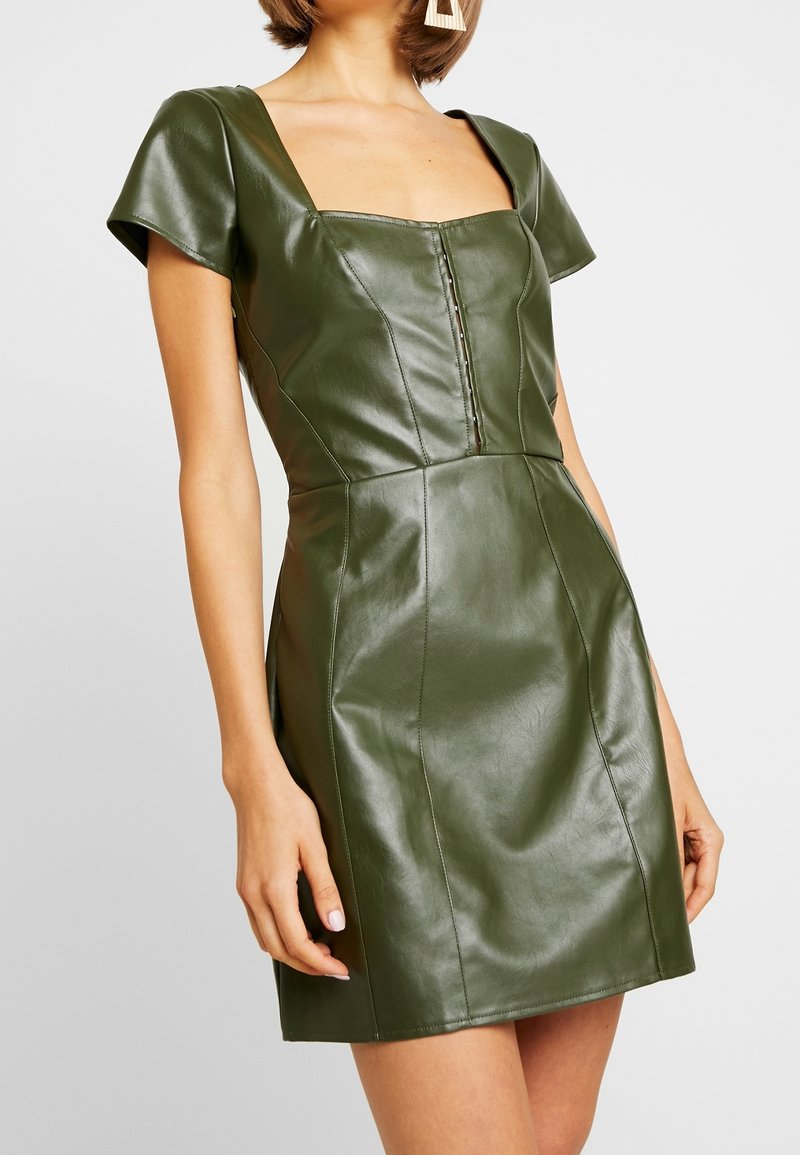 Grünes Kunstlederkleid mit quadratischem Ausschnitt, kurzen Ärmeln und einer taillierten Silhouette mit Knopfdetails und Nähten an der Vorderseite.