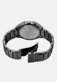 Sat s od nehrđajućeg čelika s brušenom završnom obradom, osmerokutnim kućištem i narukvicom u stilu narukvice. Sadrži kopču na preklop i glatku, ugraviranu poleđinu.