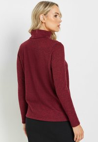 Burgundy polokrage tröja med långa ärmar, mjukt texturerat tyg och en åtsittande design, med en mittsöm på baksidan.