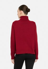 Rød rullekrave sweater lavet af strikket stof med ribbede manchetter og kant, der har en afslappet pasform og sænkede skuldre.