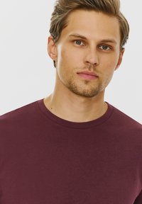 Burgundowa koszulka typu crew-neck z krótkimi rękawami, wykonana z miękkiego, gładkiego materiału, charakteryzująca się prostym wzornictwem, bez widocznych wzorów czy logo.