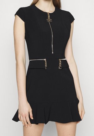 Robe noire à manches courtes avec des fermetures éclair argentées à l'avant et à la taille, ornées de tirettes en chaîne dorée, et un ourlet à volants.