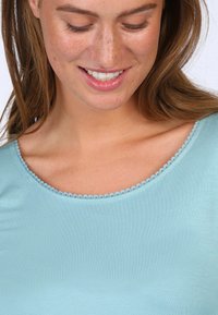 Hellblaues Kurzarmoberteil mit glatter Textur und rundem Ausschnitt mit dekorativem gewelltem Saum.