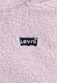 Pink fleece fabric close-up featuring a black Levi's logo tag, showcasing soft, textured material with a cozy appearance.