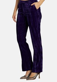 Pantaloni in velluto viola con righe verticali, tasche anteriori e taglio dritto, abbinati a scarpe con tacchi a spillo argentate.