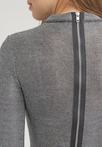 Top in tessuto effetto texture in bianco e nero con una zip argentata prominente sul retro, dotato di un collo liscio e un design aderente.