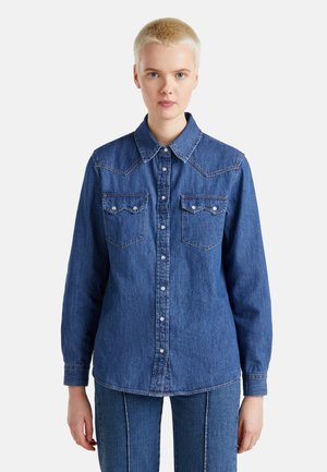 Blaues Jeanshemd mit langen Ärmeln, durchgehender Knopfleiste, spitzem Kragen, zwei Brusttaschen und markanten Ziernähten am Yoke.
