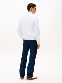 Sweatshirt branco com gola alta, combinado com calças azul-escuras. As calças são de corte largo com um design casual e sapatos castanhos.
