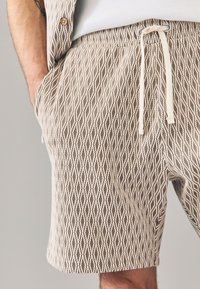 Herenkorte broek met een geometrisch diamantpatroon in beige en crèmekleur, elastische tailleband met verstelbare trekkoord, voorzien van zijzakken.