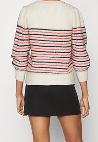 Maglione crema pallido con righe orizzontali nere e corallo, maniche a sbuffo e polsi a coste. Abbinato a una gonna nera attillata.