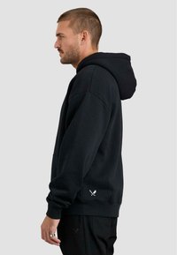 Felpa nera con cappuccio e tasca a marsupio. Presenta una vestibilità comoda, polsini a costine e dettagli ricamati sull'orlo. Tessuto morbido.