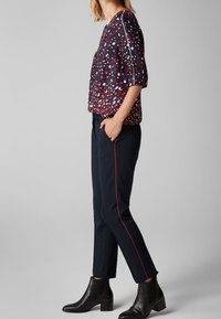 Blouse florale navy avec des accents rouges et blancs, associée à un pantalon navy ajusté avec des rayures latérales rouges. Le modèle porte des bottines noires.