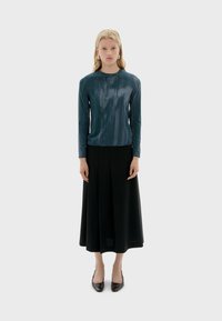 Teal lange mouwen top met een subtiele textuur, gecombineerd met een zwarte vloeiende rok. Het model staat in donkere schoenen tegen een lichte achtergrond.