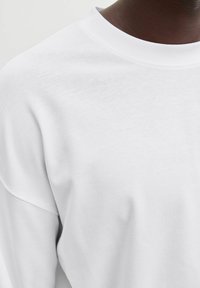 Hvid sweatshirt med rund hals, der har en blød tekstur og sænkede skuldre. Stoffet virker glat og behageligt.