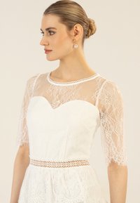 Witte kanten jurk met een sweetheart-halslijn, doorschijnende kanten mouwen en een taille met kantafwerking. Geweven bloemmotieven door het hele ontwerp.