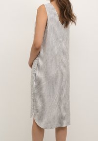 Vestido sin mangas, a la altura de la rodilla en blanco con rayas verticales en navy; presenta un diseño de espalda en V y bolsillos laterales; hecho de una tela ligera.