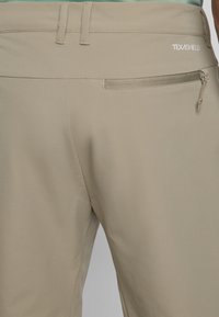 Beige Hosen aus glattem, dehnbarem Stoff. Mit einer Reißverschlusstasche auf der rechten Seite und auffälliger Naht am Bund.