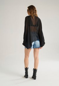 Black sheer blouse with long sleeves, featuring lace accents, paired with denim shorts and black heeled boots. Simple and modern silhouette.