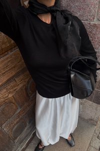 Čierna blúzka s dlhými rukávmi, biela voľná sukňa, čierna kožená kabelka a čierne viazacie baleríny; doplnené priesvitným čiernym šálom.