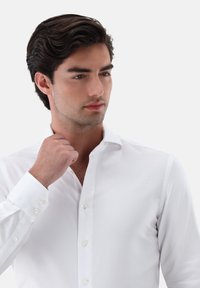 Camicia bianca a maniche lunghe con bottoni, realizzata in un tessuto testurizzato, con colletto a punta e polsini rotondi, chiusa con bottoni bianchi.