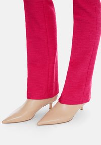 Narrow pink textured trousers paired with pointed nude kitten heels, showcasing a smooth leather finish and a subtle heel design.