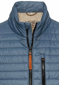 Blauer Puffy-Jacke mit hohem Kragen, mit Zickzack-Steppung, einem zentralen Reißverschluss und einer Brusttasche mit Reißverschluss und Lederakzent.