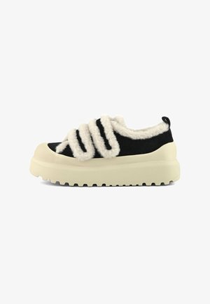 Baskets noires avec une semelle épaisse crème et trois bandes velcro crémeuses et duveteuses, dotées d'une languette de traction au niveau du talon.