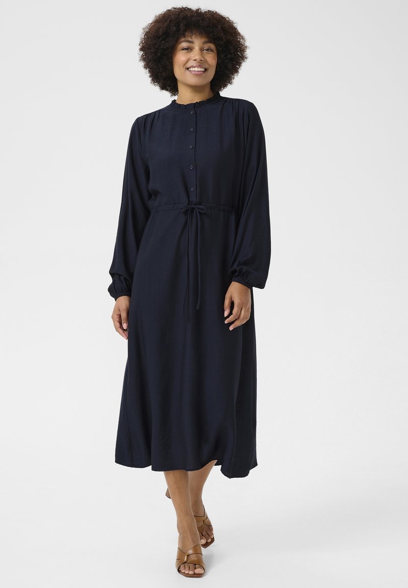Námornícke šaty s dlhým rukávom a predným zapínaním na gombíky, s volánovým golierom, stiahnutým pásom a splývavou sukňou v tvare písmena A. Hladká textúra, minimálny dizajn.