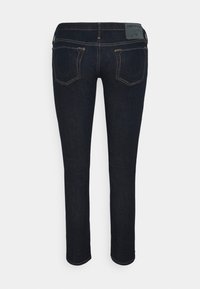 Jeans de mezclilla azul oscuro con corte slim, que presentan costuras amarillas, una cintura alta y bolsillos traseros con acentos decorativos.