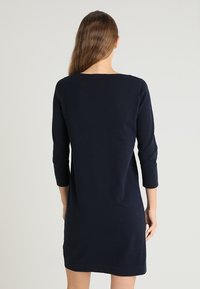 Námořnická modrá šaty ke kolenům vyrobené z měkké tkaniny, s rukávy po tři čtvrtiny a kulatým výstřihem, s jednoduchým a elegantním designem.