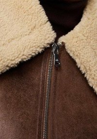 Brązowa kurtka z owczej wełny z kołnierzem w kolorze kremowym, z metalowym zamkiem z przodu i przyjemną w dotyku fakturą.