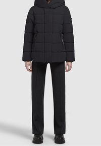 Musta untuvatakki hupulla, jossa isokokoisia tikattuja osioita ja sivuvetoketjut. Yhdistetty mustiin istuviin housuihin ja paksupohjaisiin mustiin saappaisiin.