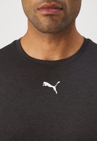 Zwarte korte mouwen shirt van zacht materiaal met een witte springende puma-logo op de linkerborst. Ronde halslijn, subtiele textuur.