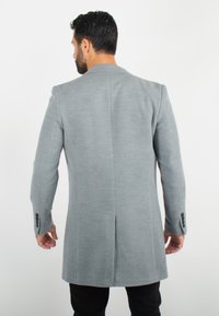 Manteau en laine grise avec une coupe droite, des épaulettes et une fente unique à l'arrière. Doté de boutons noirs aux poignets.