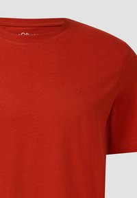 Rotes Baumwoll-T-Shirt mit Rundhalsausschnitt, kurze Ärmel und einem kleinen prägenden Logo auf der Brust. Glatte, gleichmäßige Textur über das gesamte Shirt.